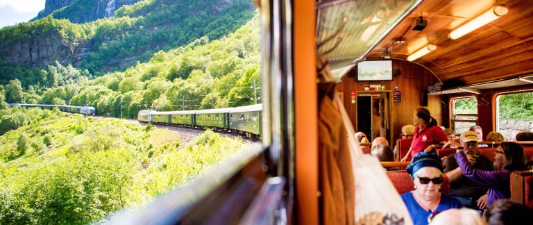 People sitting inside train. Train is driving through beautiful green Norwegian nature.
